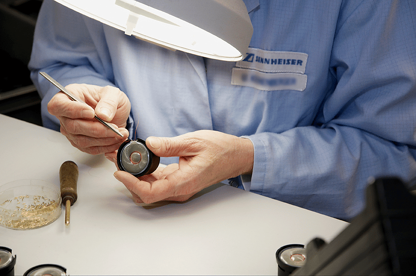 Person assembling audio equipment with a screwdriver under a lamp.