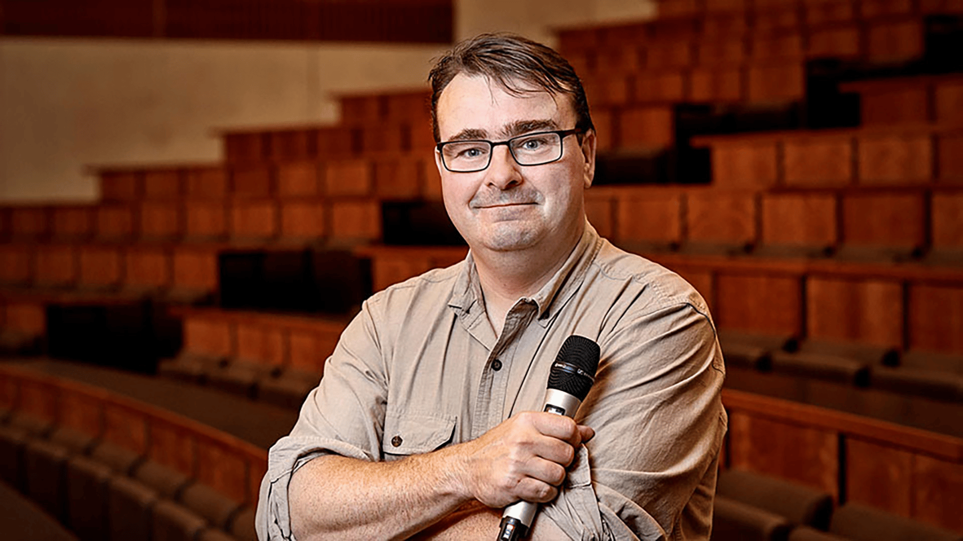 Man holding a microphone in an empty lecture hall.