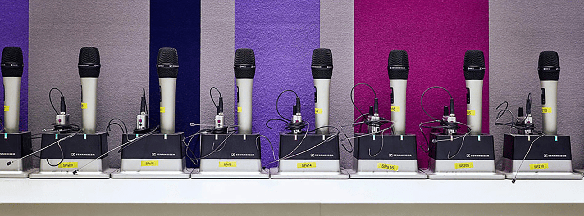 Sennheiser wireless microphones on charging stations against a colorful wall.