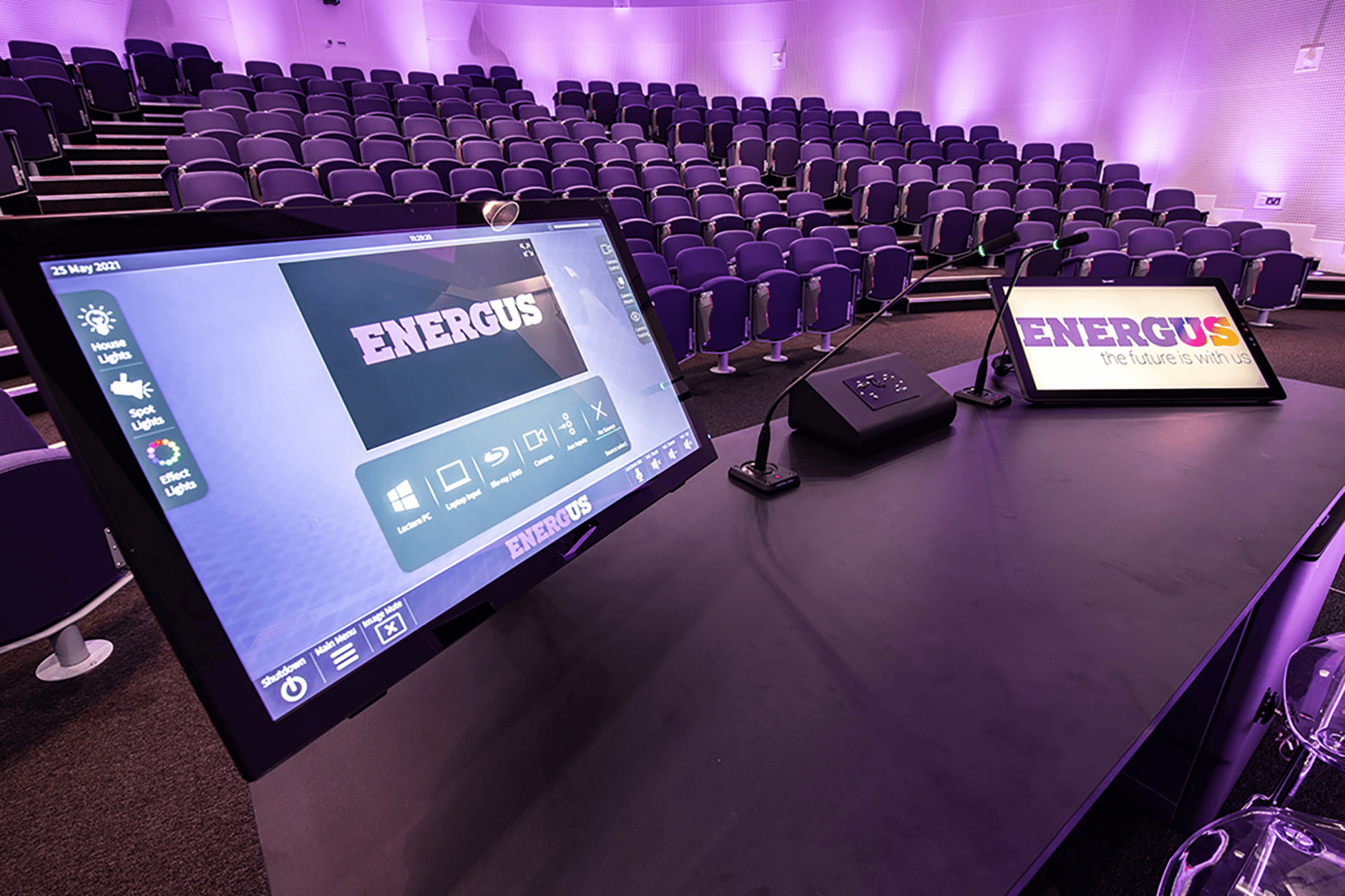 Control panel and screens in an auditorium with Energus branding.
