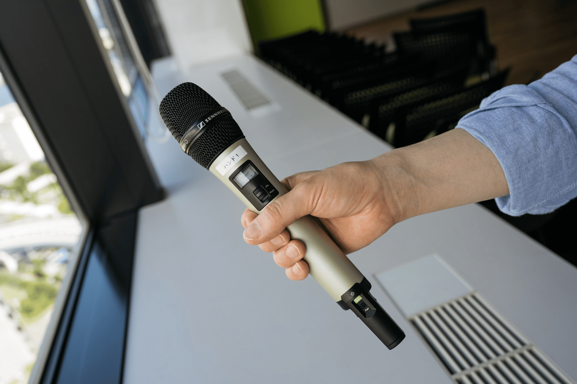 Hand holding a Sennheiser wireless handheld microphone in a modern office setting.