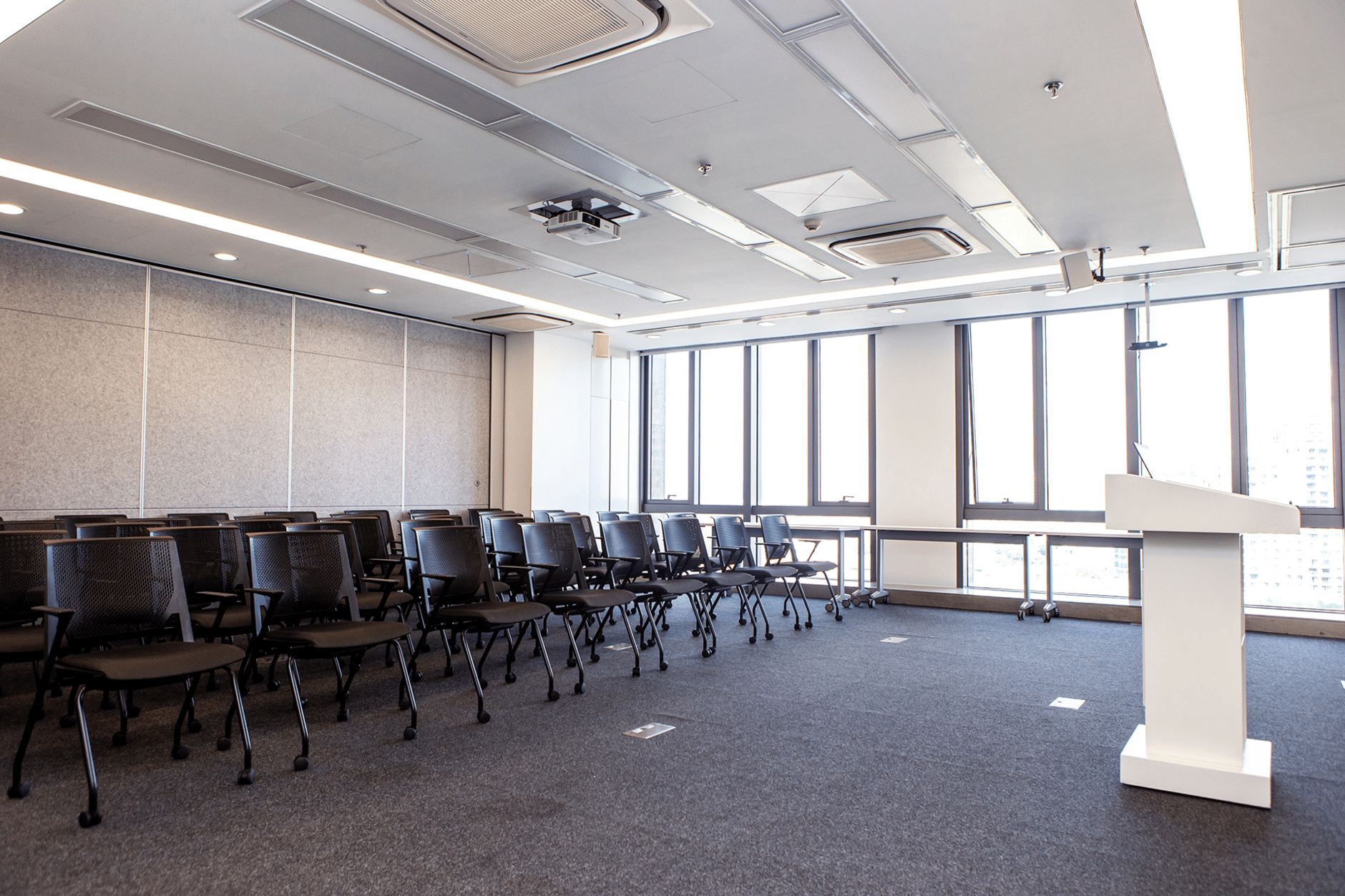 Modern meeting room with rows of black chairs and a white podium in front of large windows.
