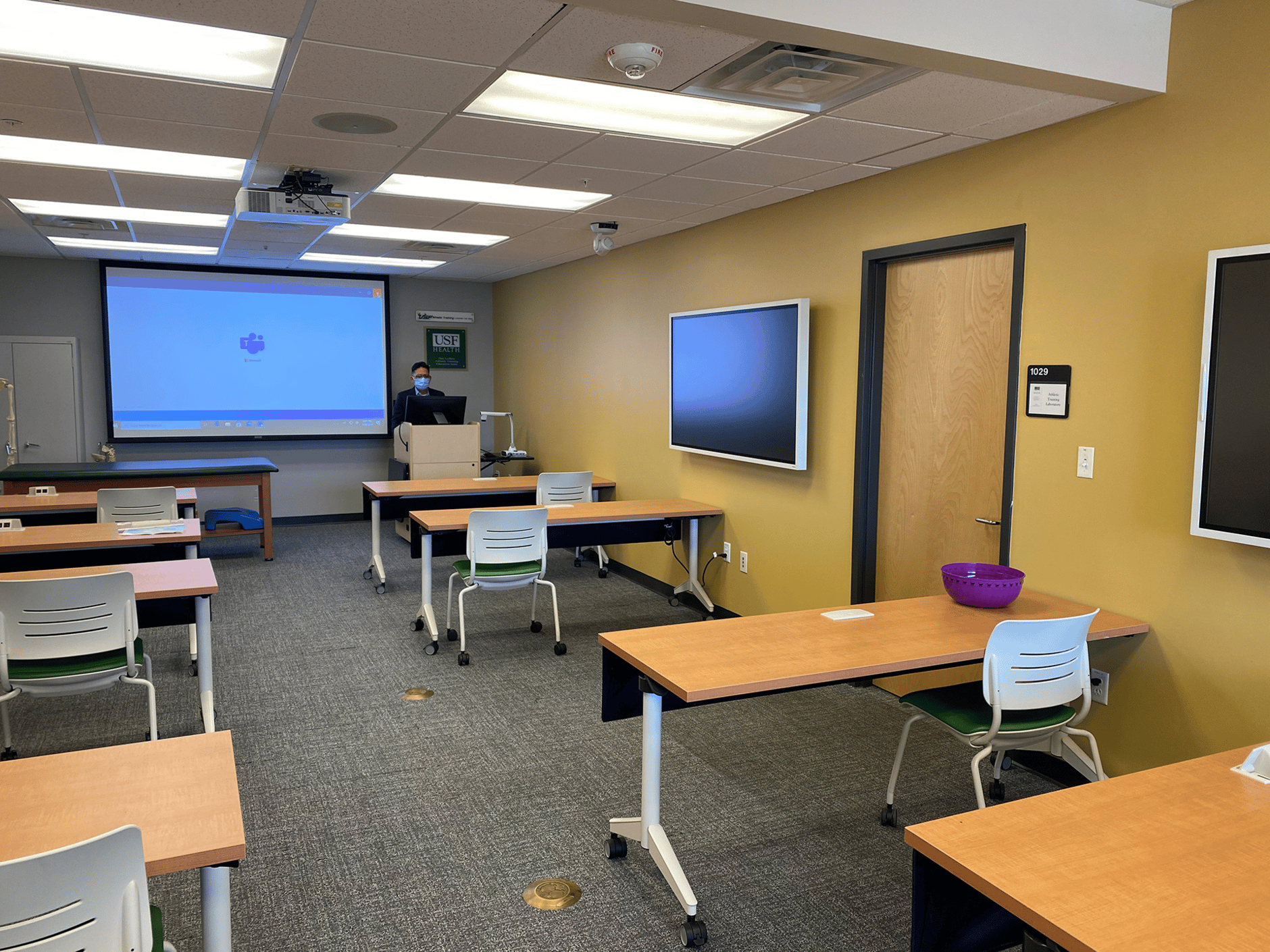 University of South Florida lecture room with desks, chairs, and a projector screen.