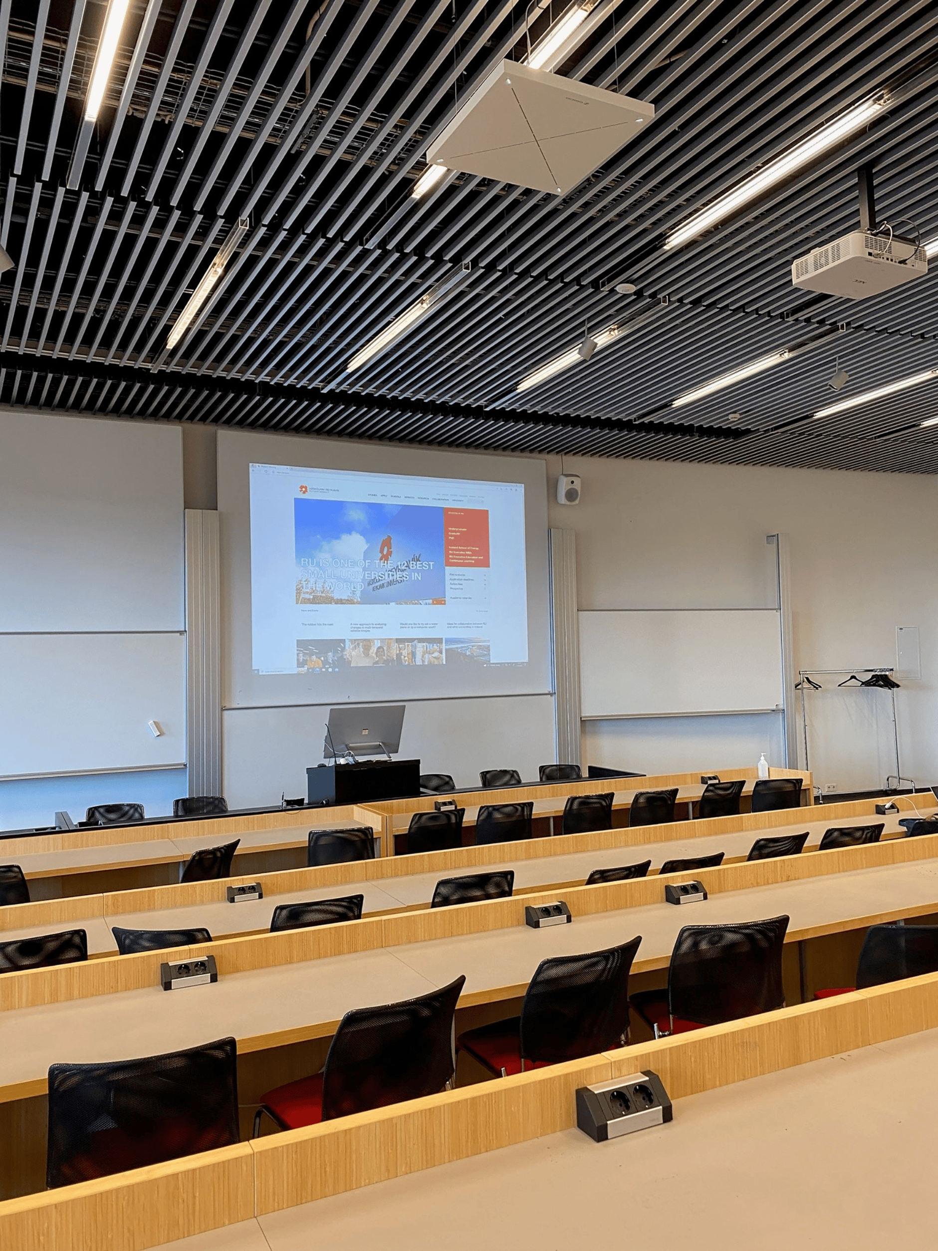 University of Reykjavik lecture room with TCC2 front view, featuring rows of desks, chairs, and a large projection screen.