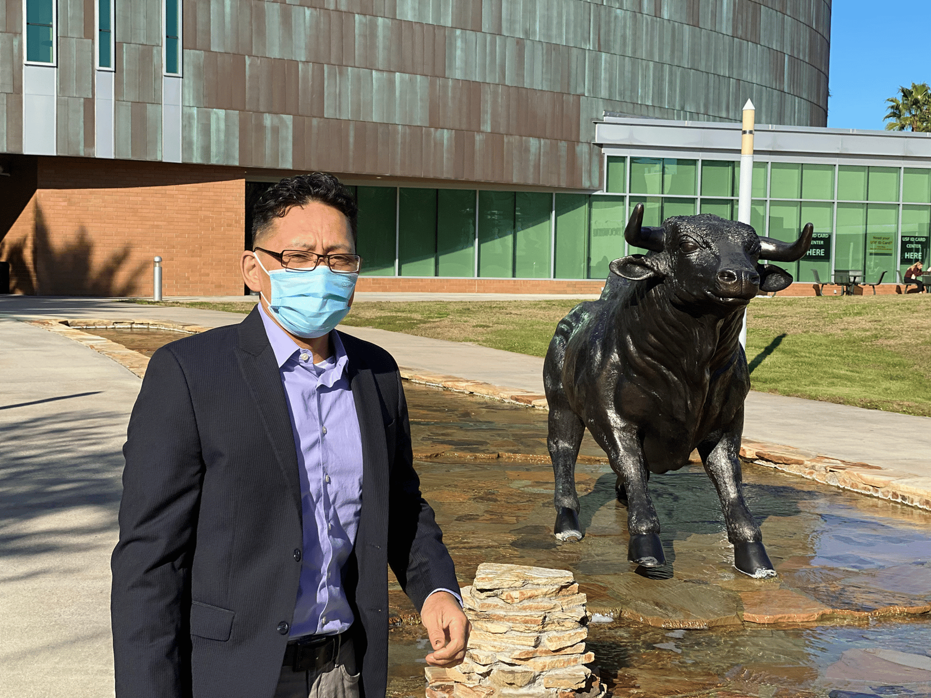 Sound engineer wearing a mask in front of the University of South Florida building and bull statue.