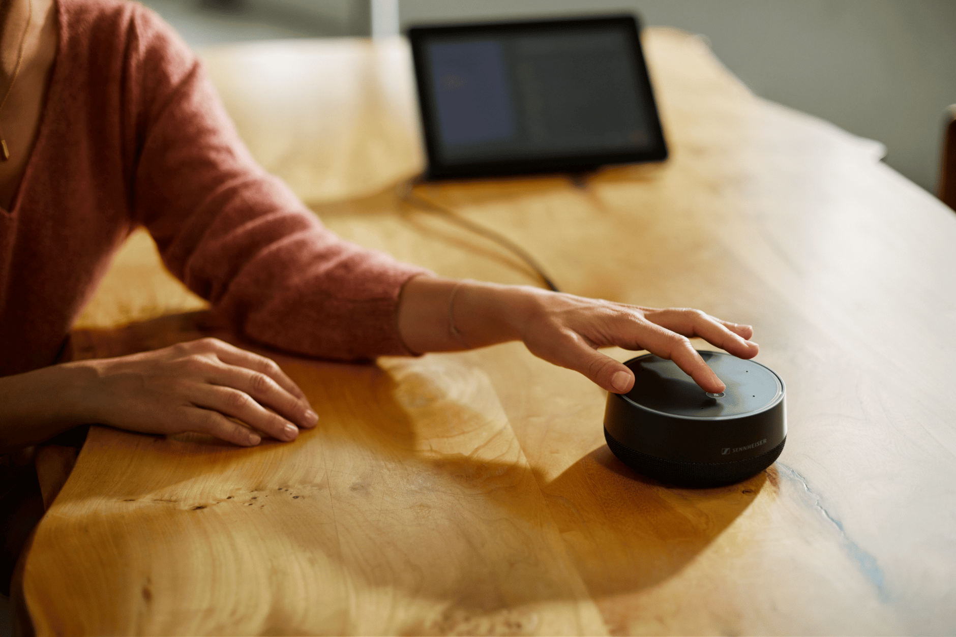 Person using Sennheiser TeamConnect device on a wooden table with a tablet in the background.