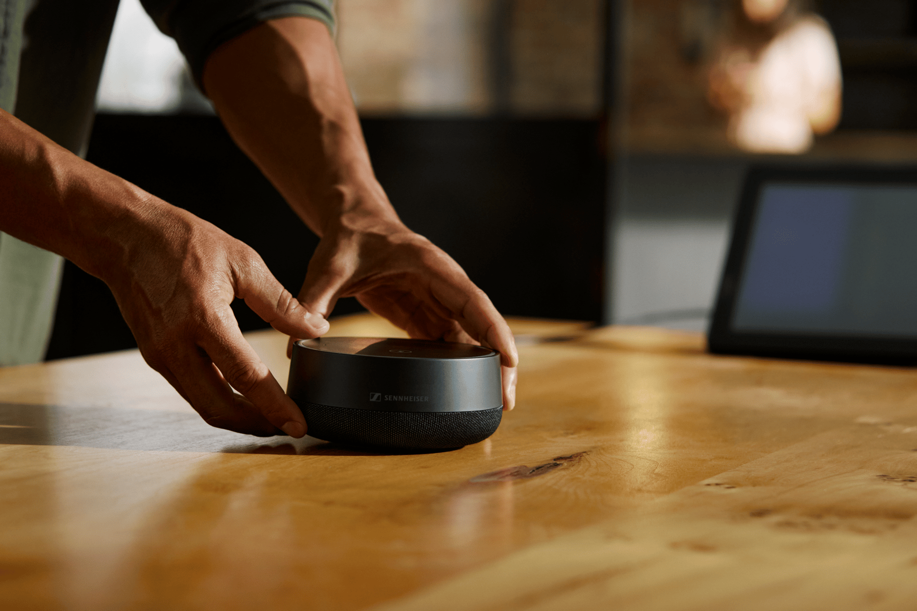 Person setting up a Sennheiser speaker on a wooden table.