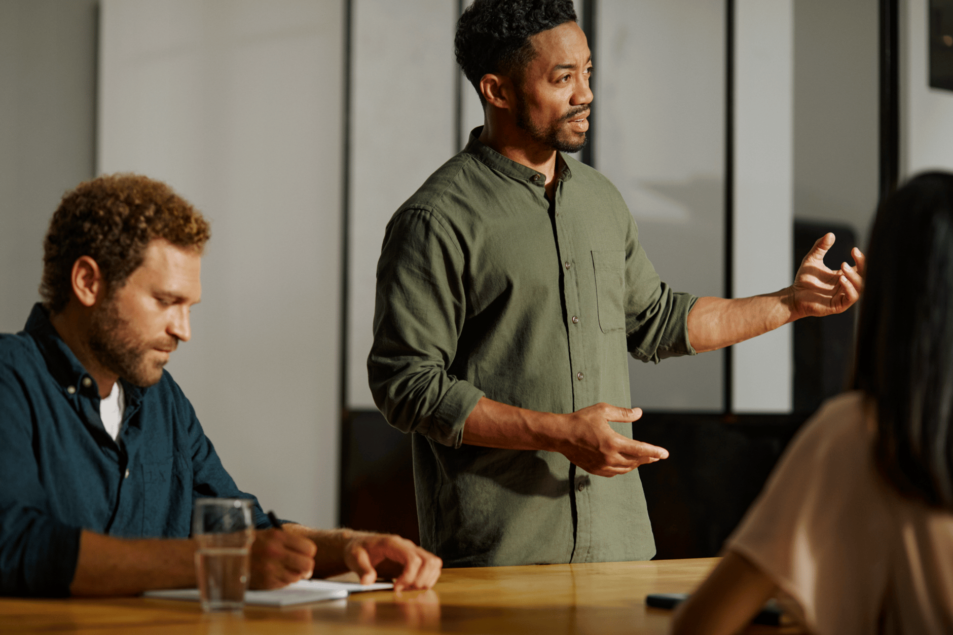 Man giving a presentation while another man takes notes in a meeting room.