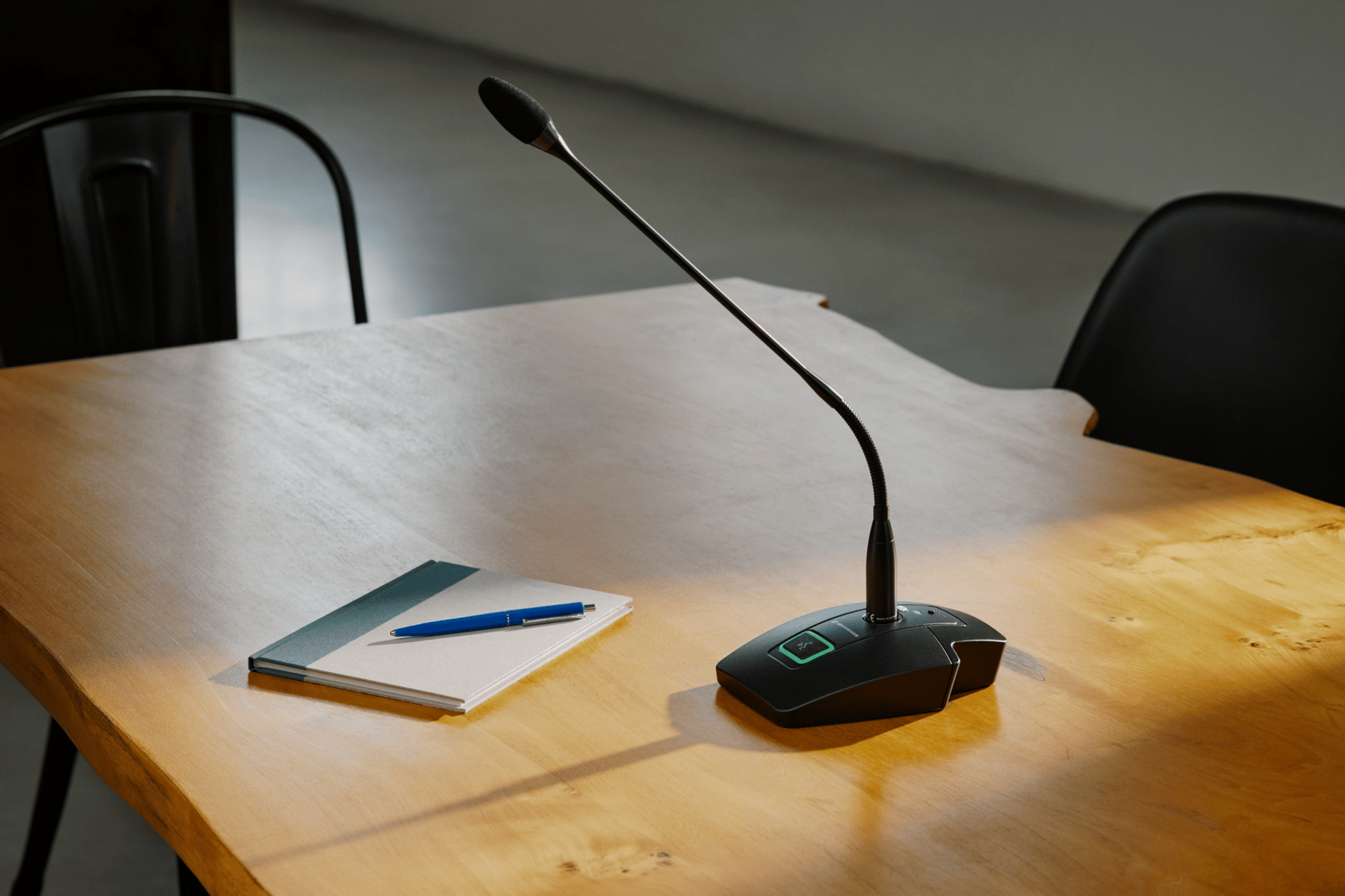Sennheiser wireless conference microphone on a wooden table with a notebook and pen.