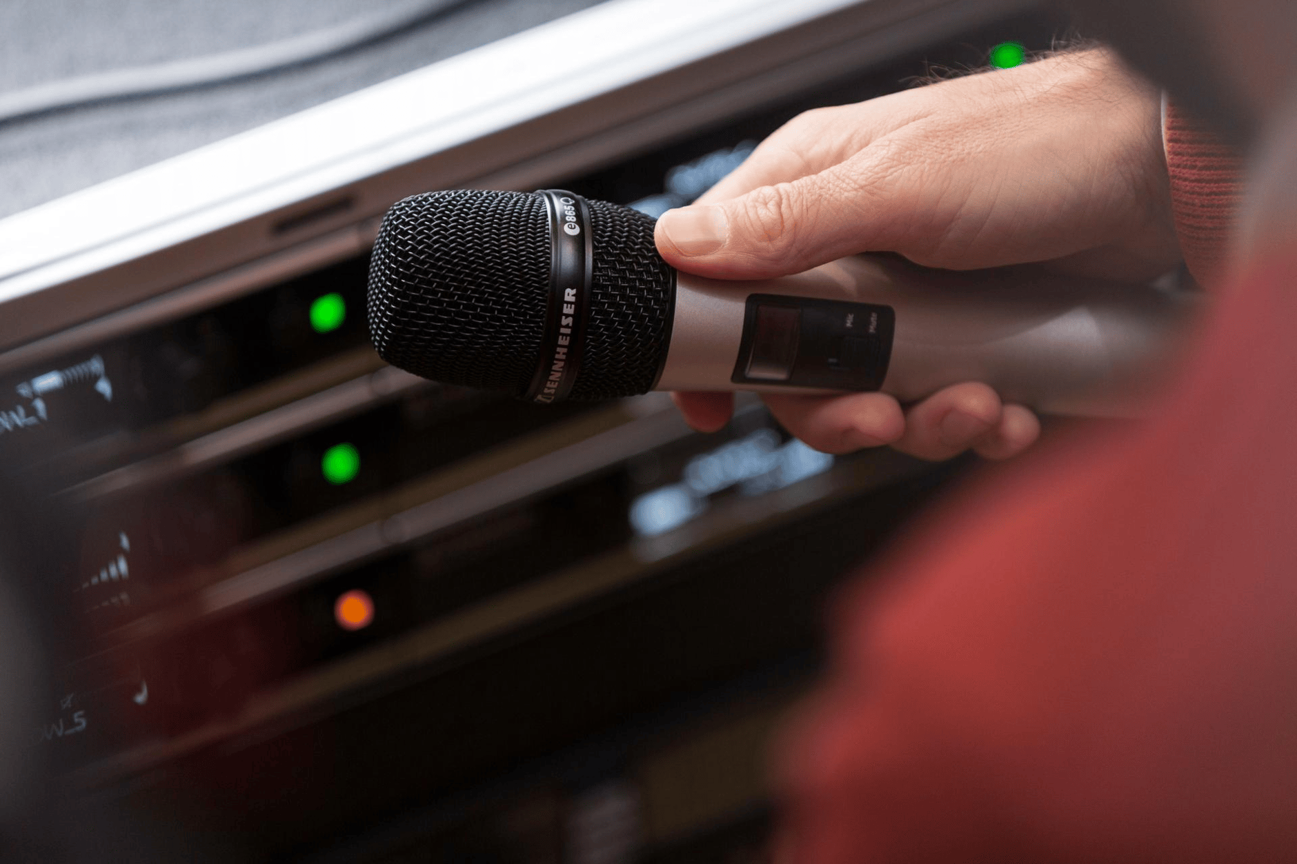 Hand holding a Sennheiser wireless microphone near audio equipment