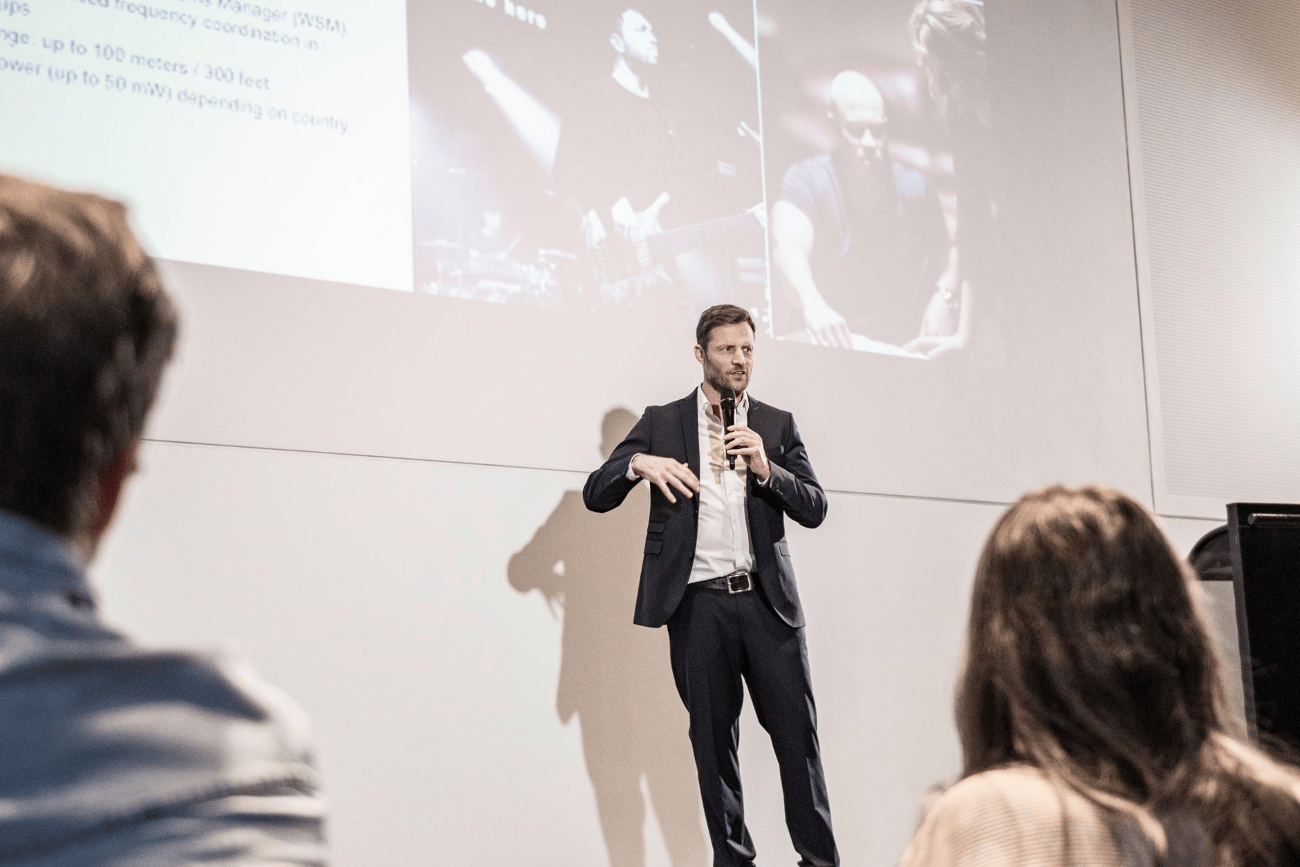 Man in a suit giving a presentation with a microphone in front of a projected screen.