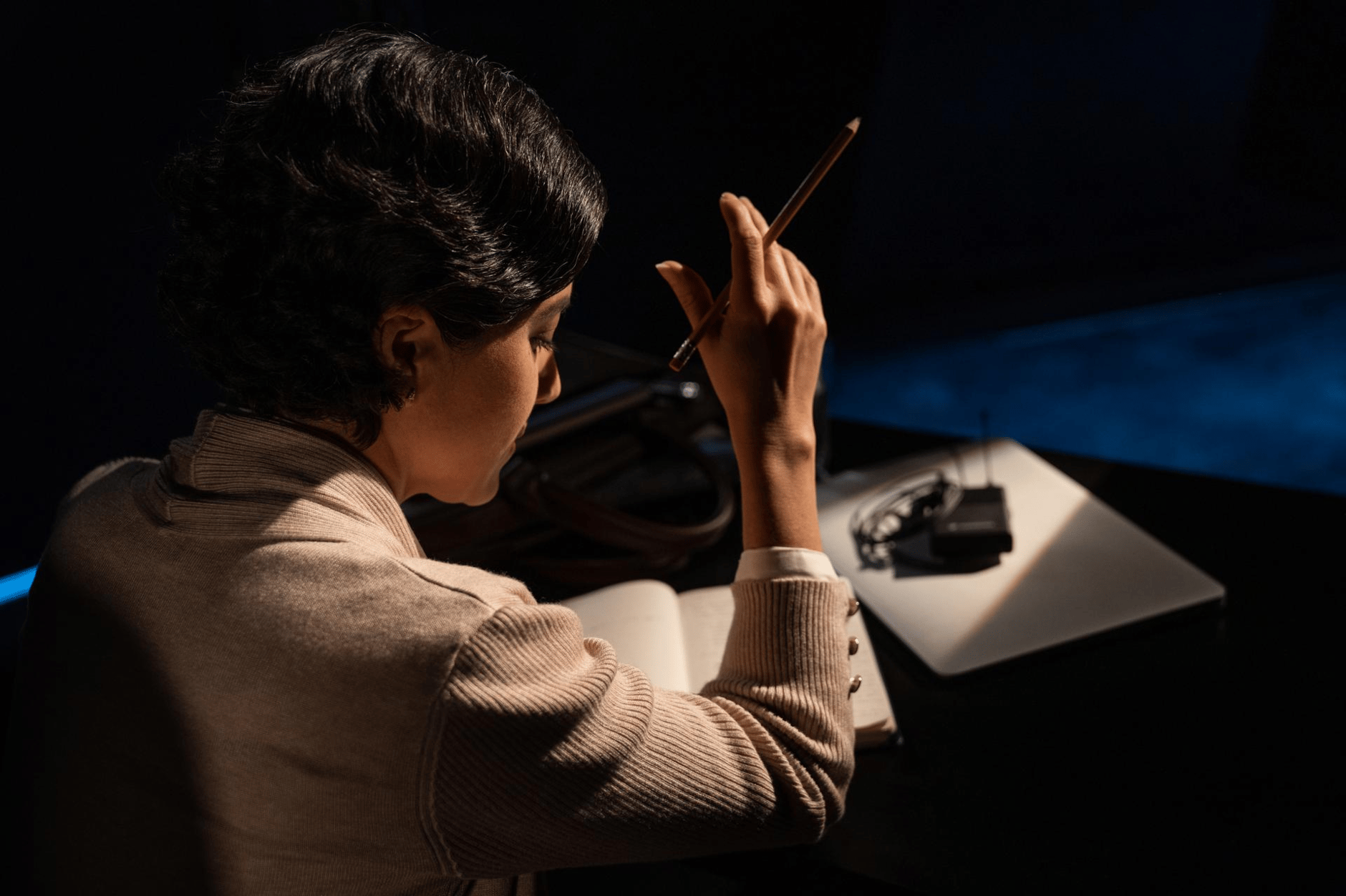 Person writing in a notebook with a pencil next to a wireless microphone system on a desk.