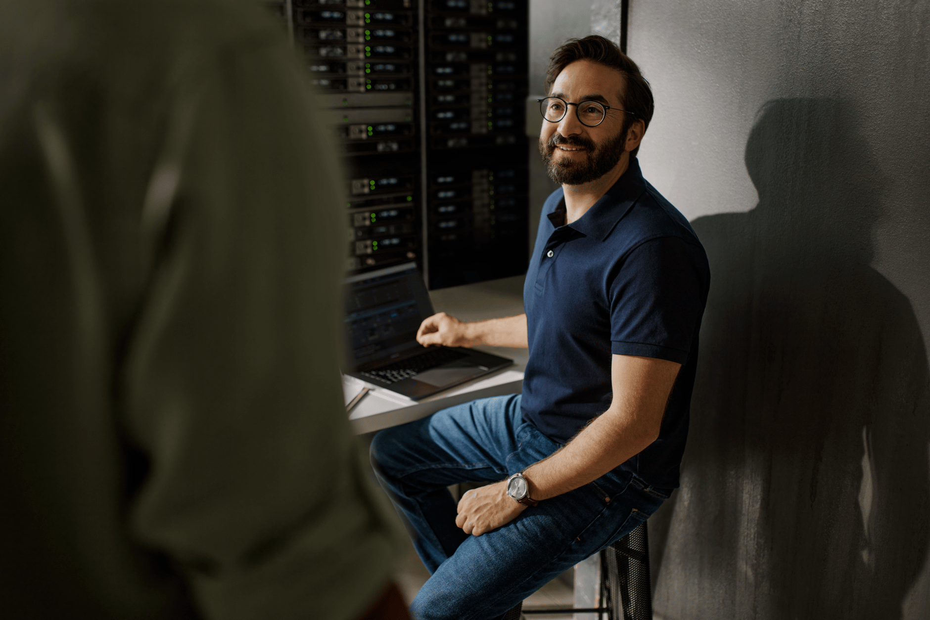 Man sitting at a desk with a laptop in a server room.