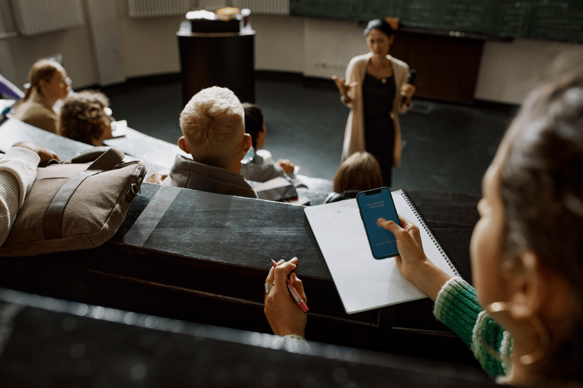 Students in a lecture hall with a professor speaking at the front.