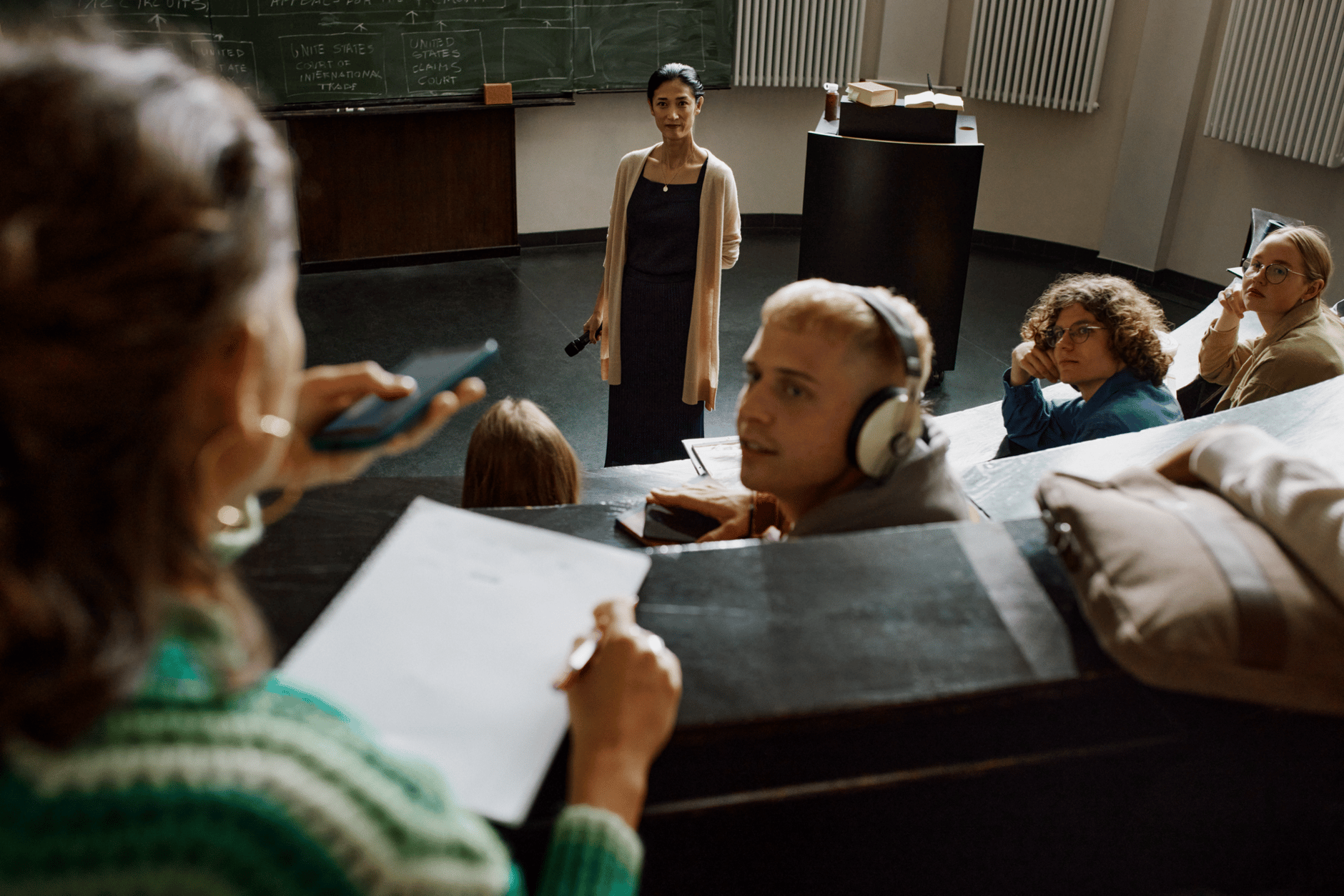 Students in a lecture hall with a professor in front of a chalkboard.