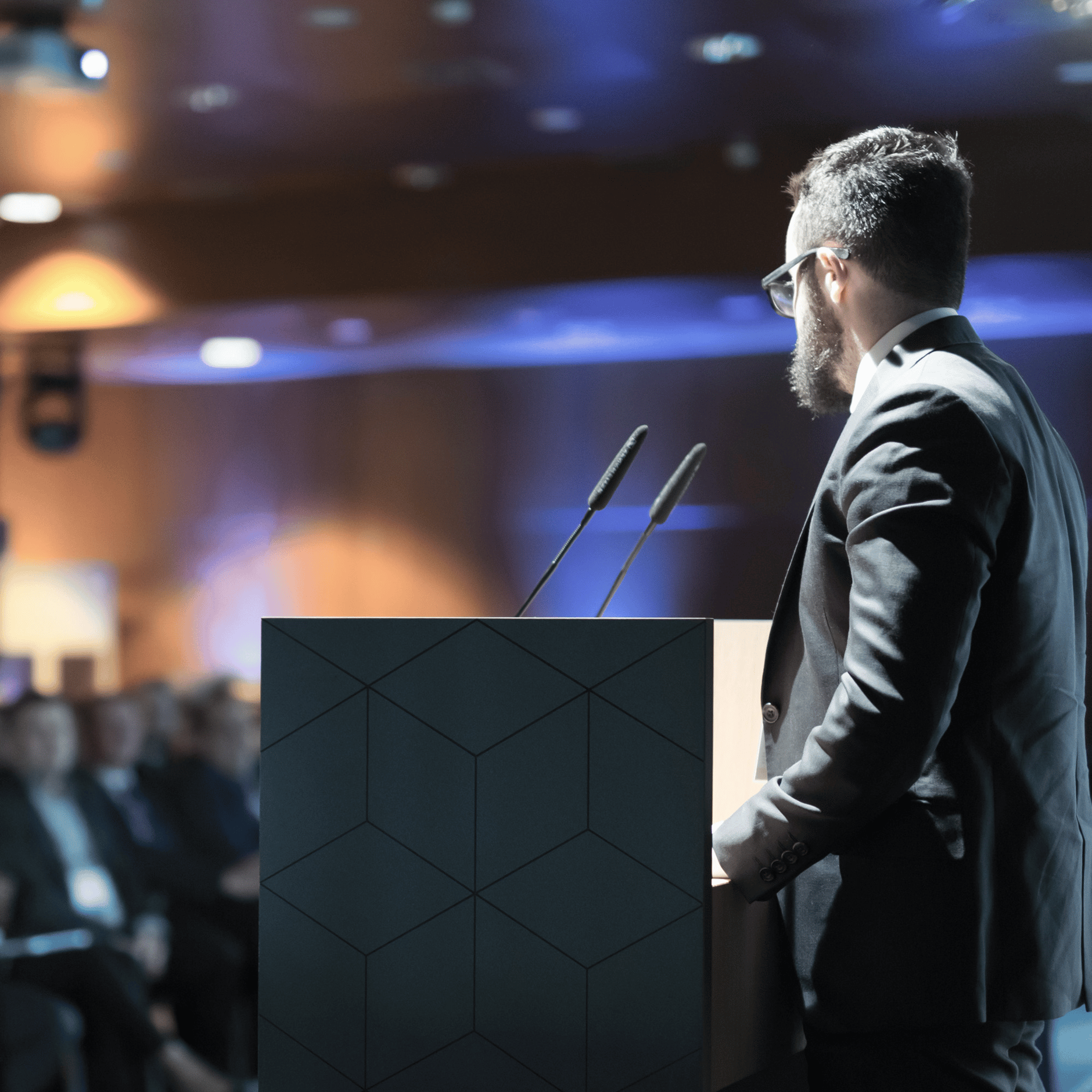 Man speaking at a conference podium with microphones in a dimly lit room.