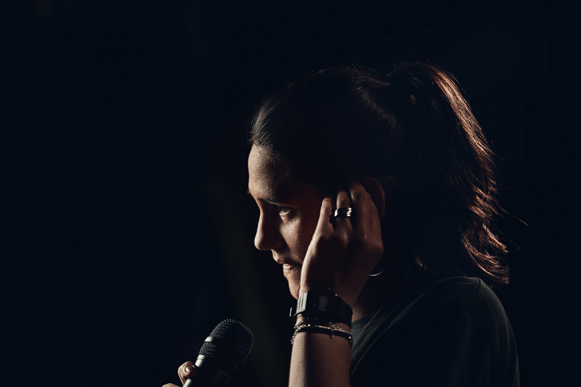 Person adjusting in-ear monitor while holding a microphone on stage.