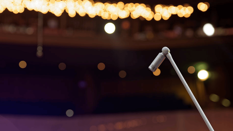 Close-up of a Sennheiser microphone on a stand with blurred stage lights in the background.