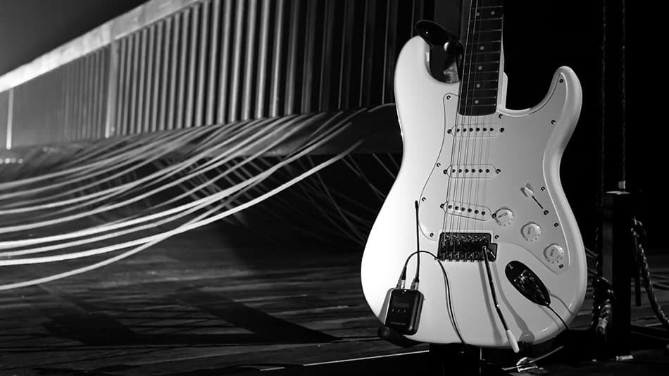 White electric guitar on stage with cables in the background.