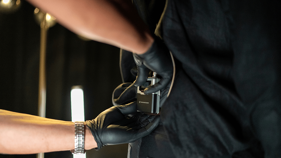 Person wearing black gloves attaching a Sennheiser microphone pack.