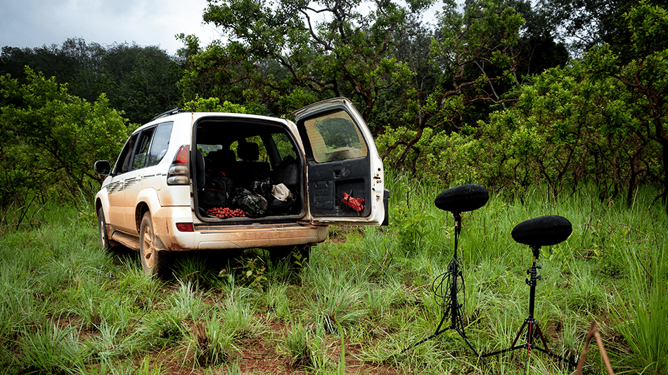 Off-road vehicle with open trunk in a grassy field next to audio recording equipment.