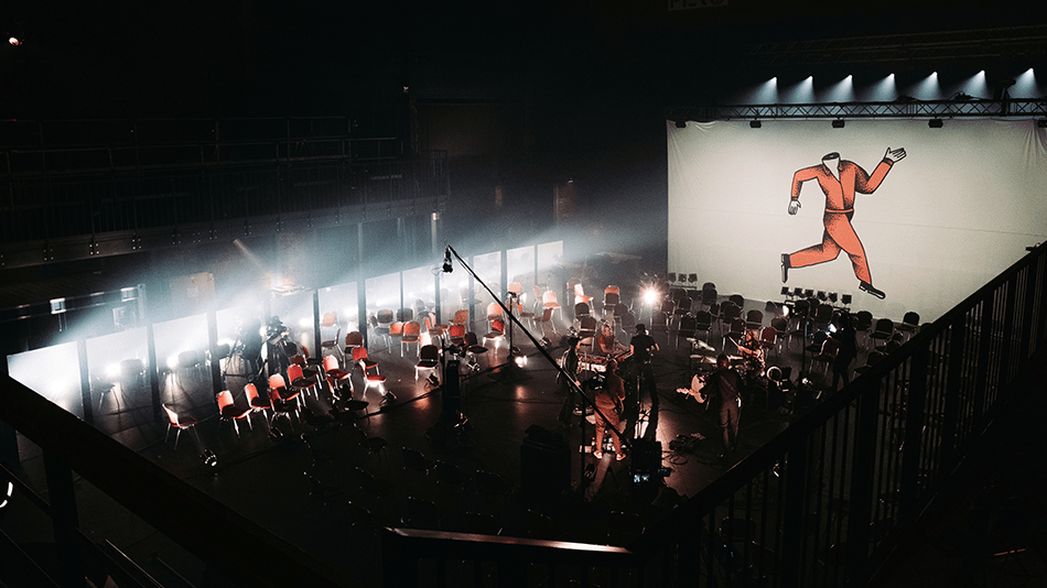 Concert stage setup with empty chairs and a large screen displaying a running man illustration.