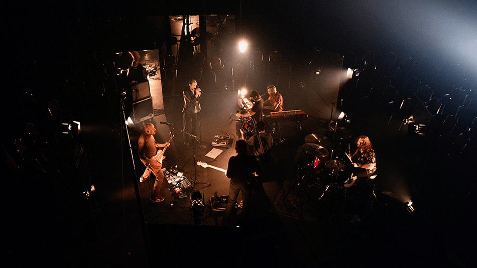 Band performing live on stage with musical instruments and dim lighting.
