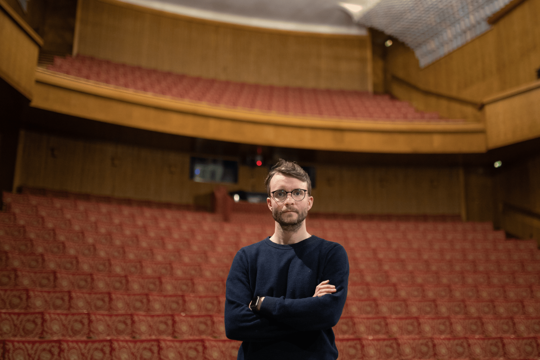 Man standing in an empty theater with red seats and wooden walls.