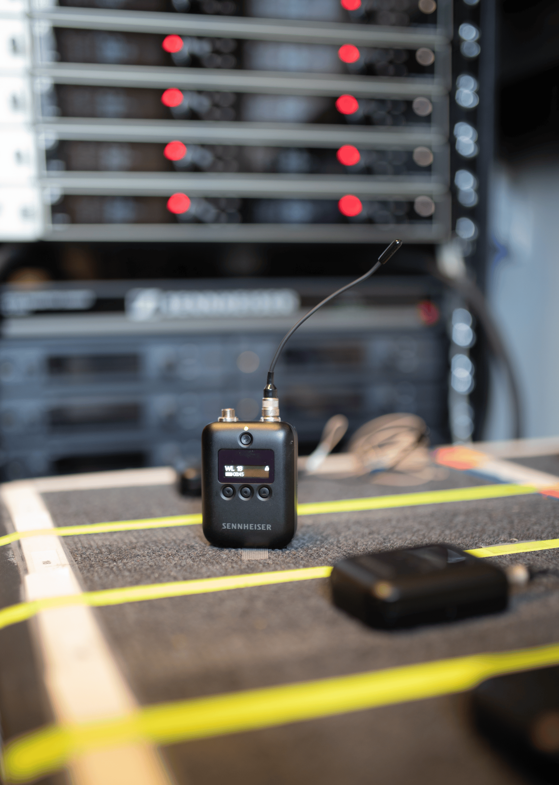 Sennheiser wireless microphone transmitter in front of audio equipment.