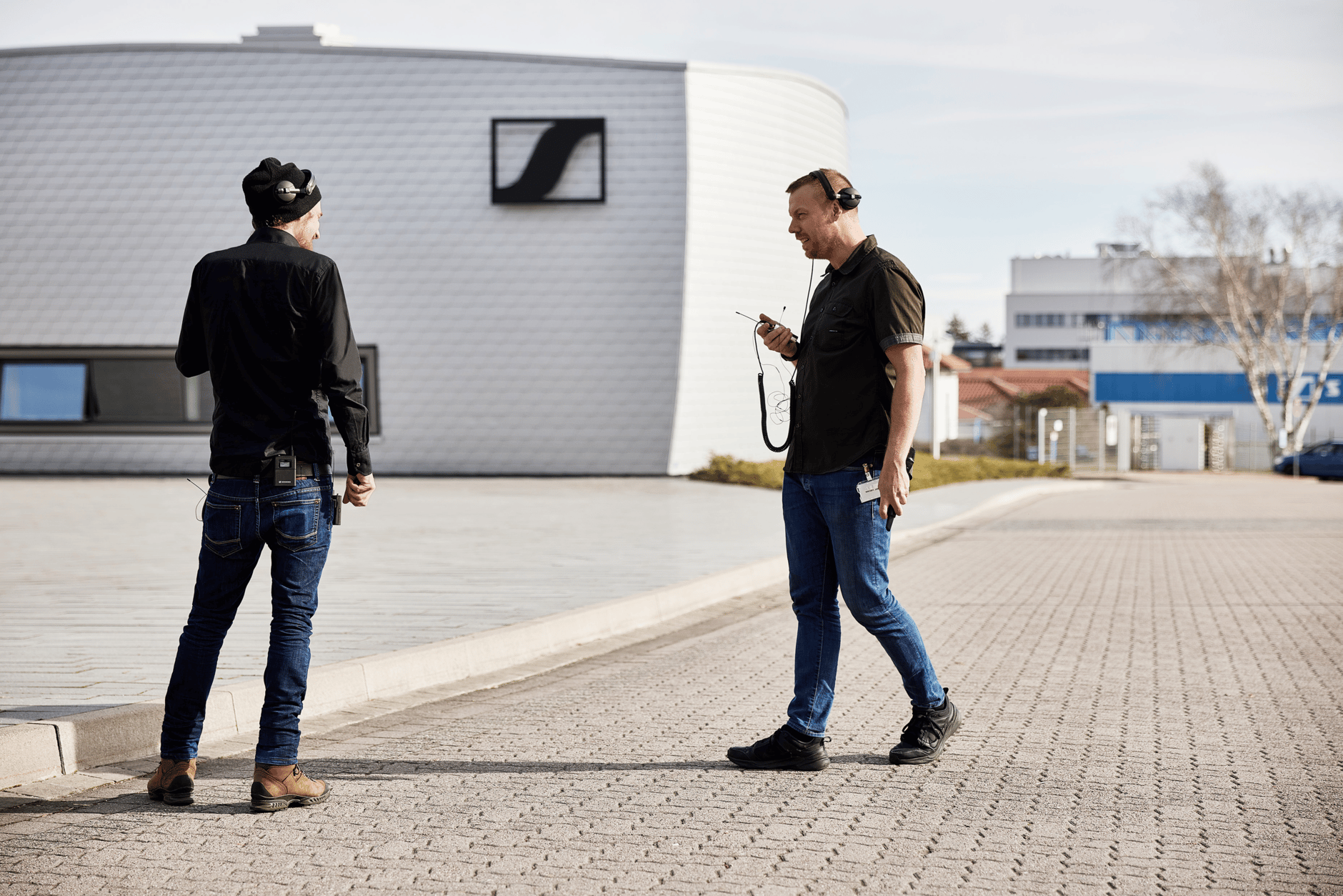 Two men using Sennheiser audio equipment outside a modern building.