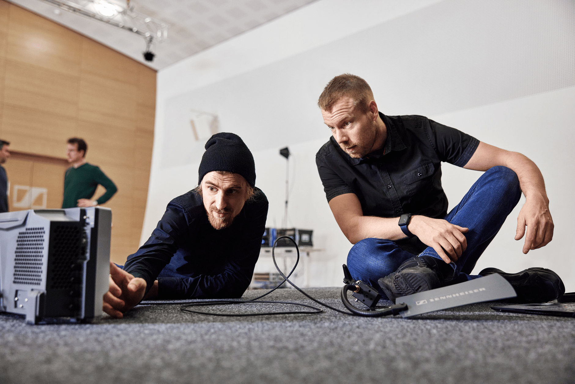Two men setting up audio equipment on the floor in a studio.