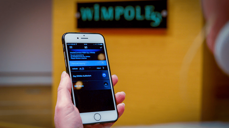 Person holding a smartphone with a hearing aid app displayed.