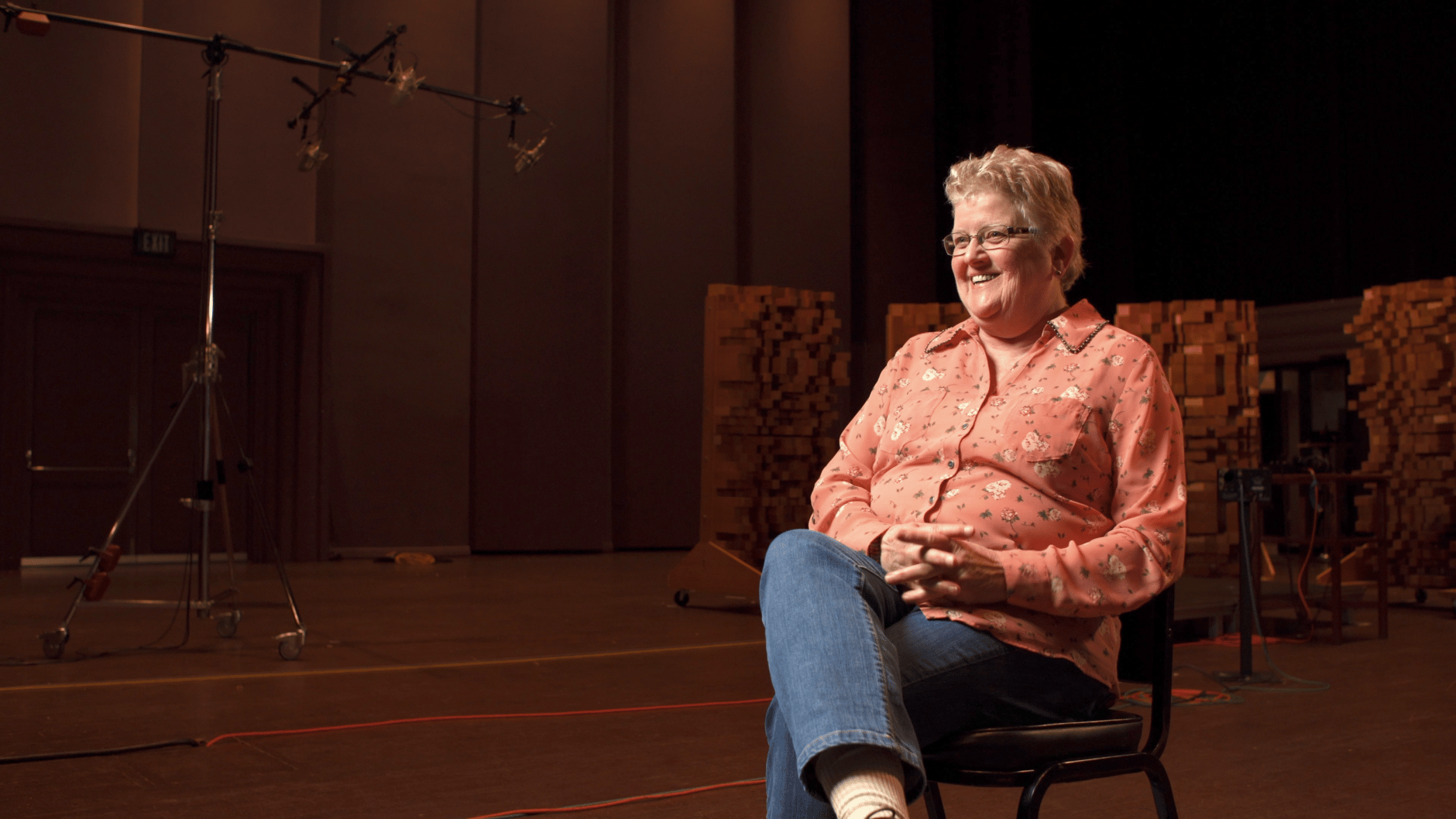 Woman in pink shirt sitting on a chair in a recording studio.