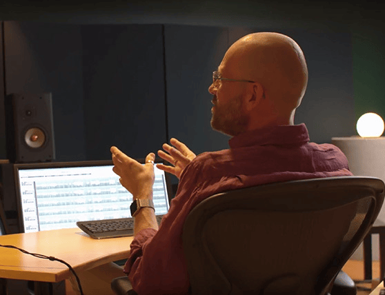 Man in a recording studio discussing audio tracks on a computer screen.