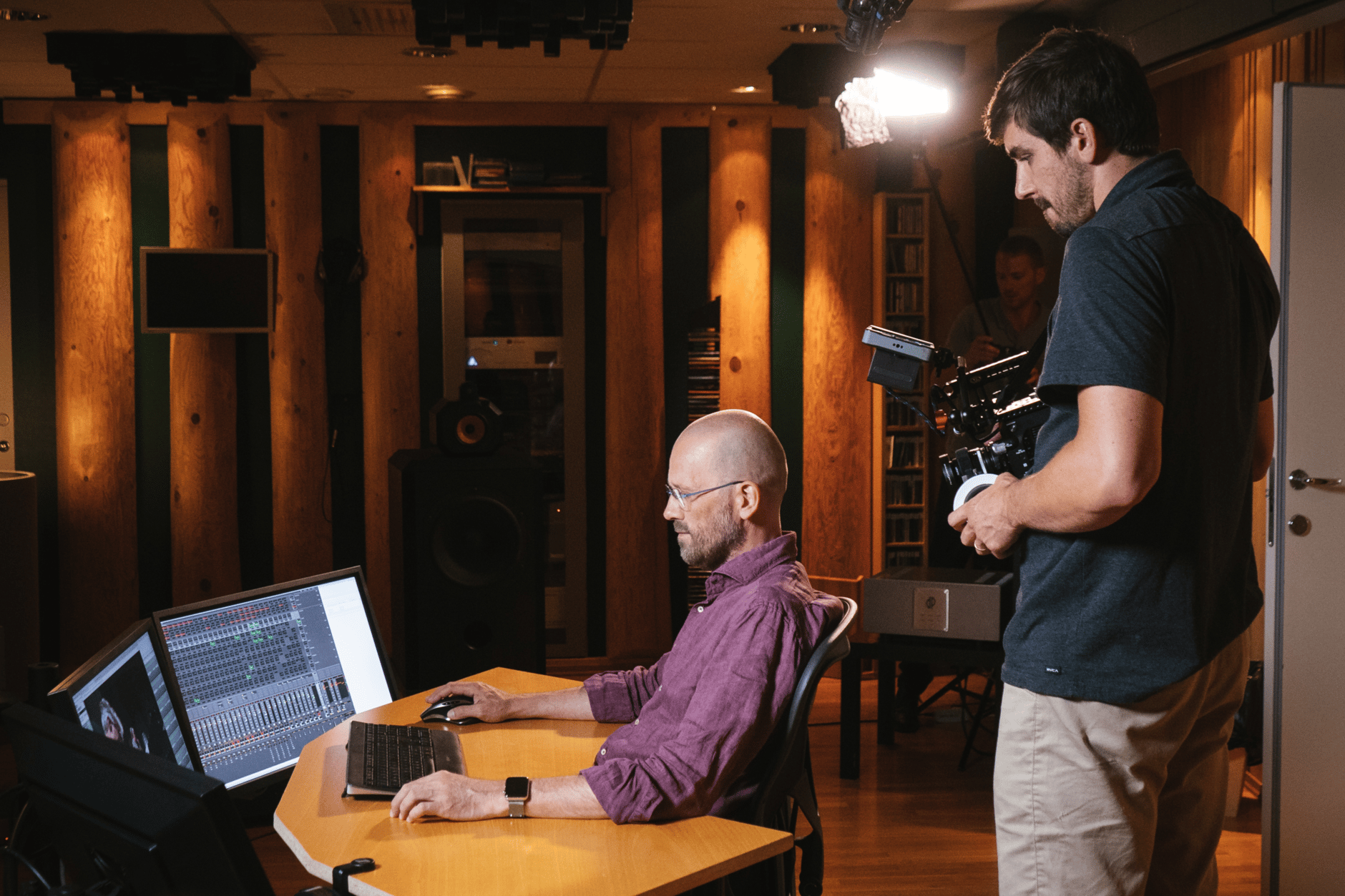 Man editing audio on computer while another man films in a recording studio.