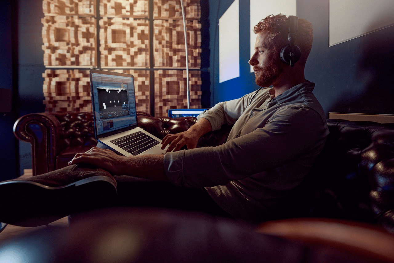 Man wearing headphones working on a laptop in a sound studio.