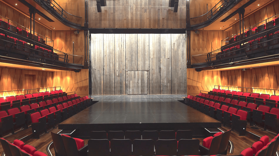 Modern theater stage with red seats and wooden interior design.