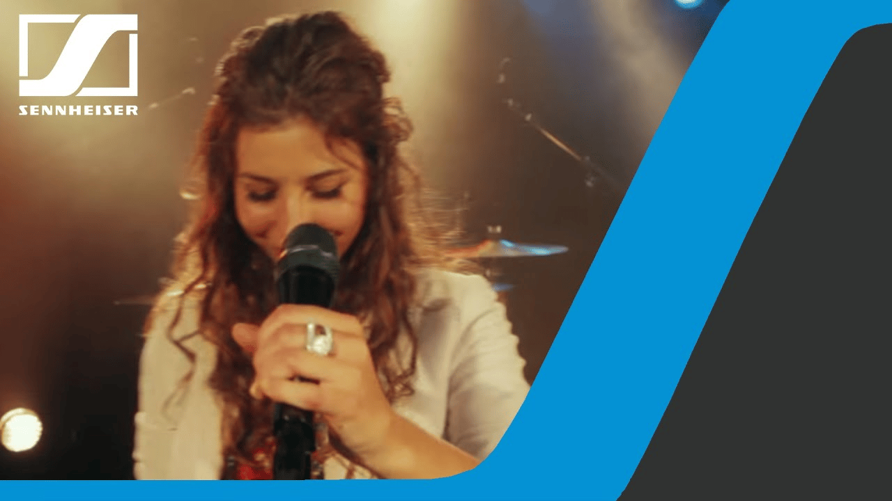 Woman singing into a Sennheiser microphone on stage with colorful lights.