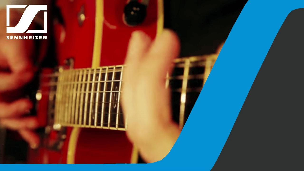 Person playing a red electric guitar with Sennheiser logo.
