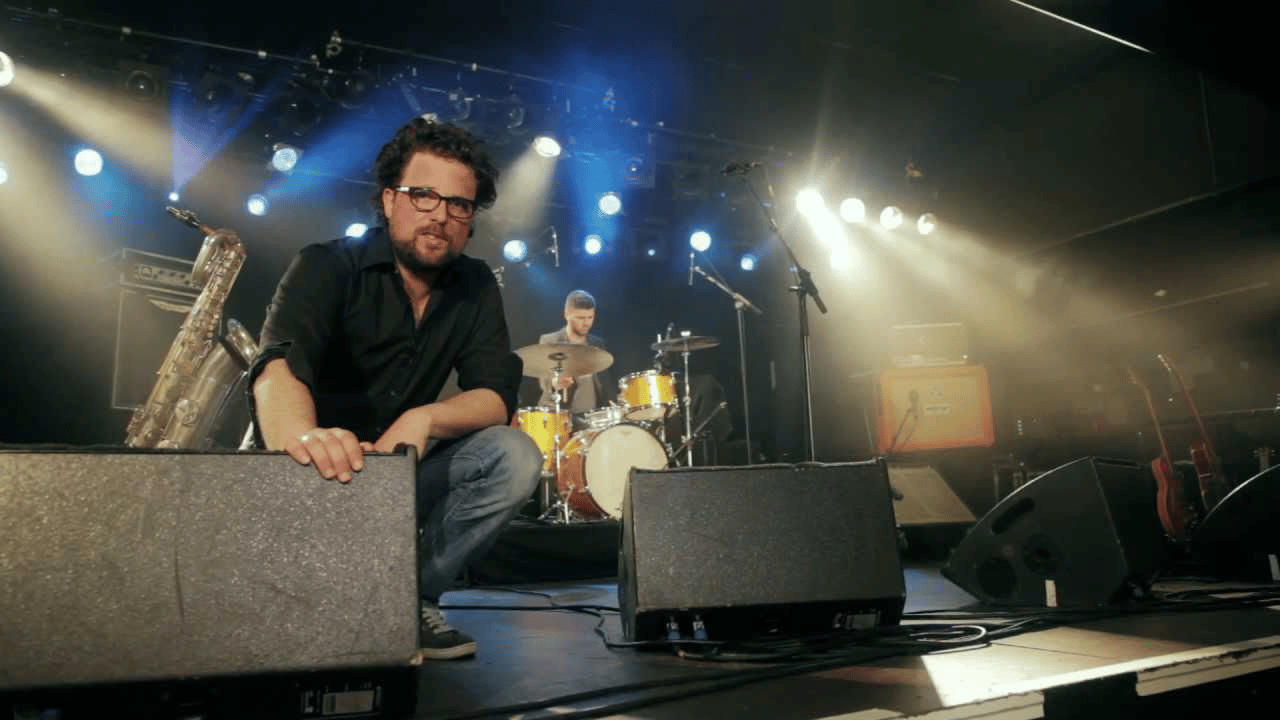 Musician setting up on stage with drum set and saxophone under bright lights.