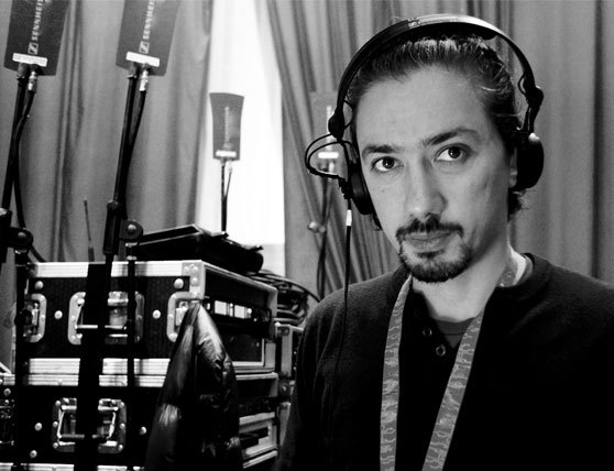 Man wearing headphones in a recording studio with audio equipment in the background.