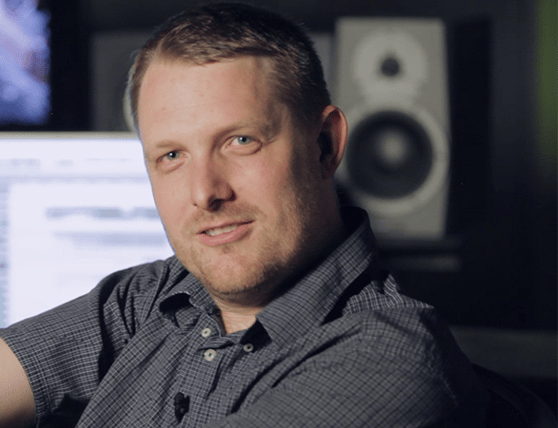 Man in a recording studio with audio equipment in the background.