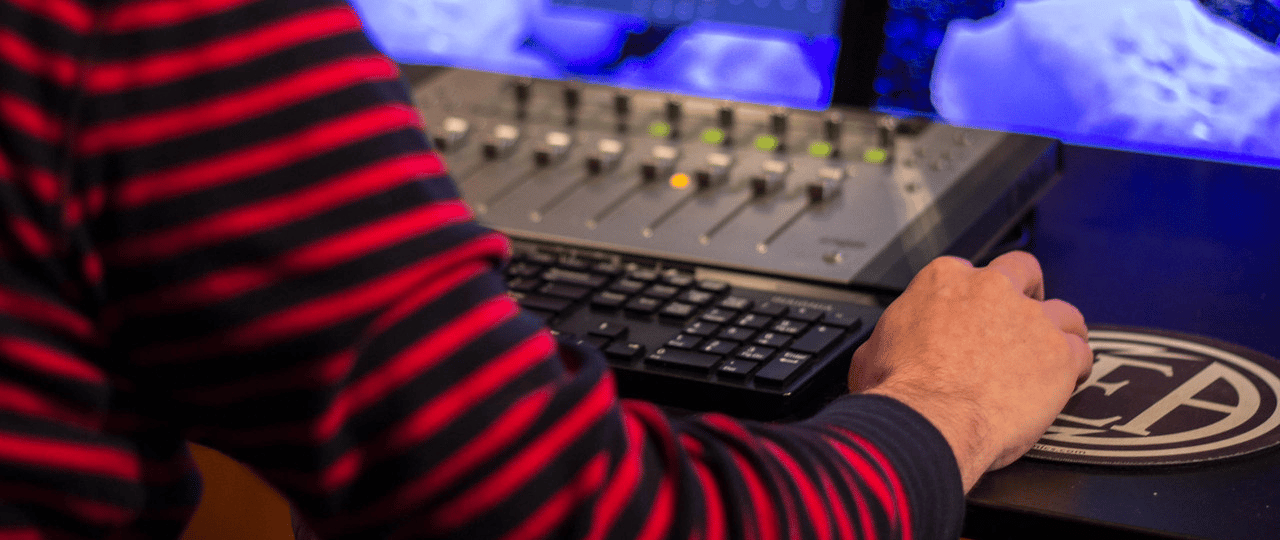 Person operating audio mixing console and keyboard in a studio.