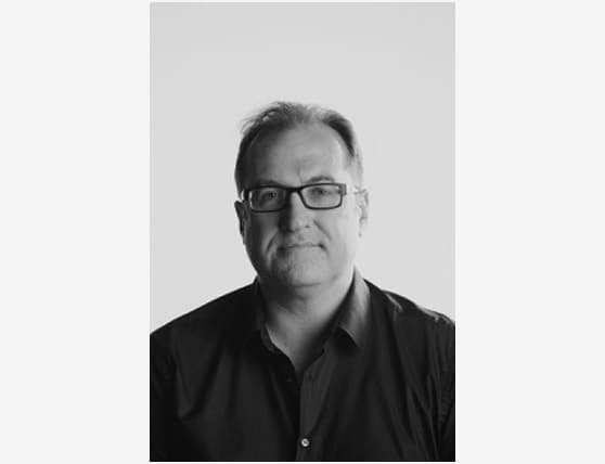 Man wearing glasses and a dark shirt against a plain background.