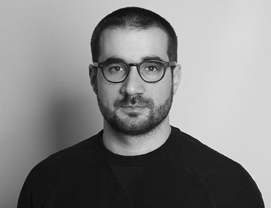 Man with glasses and beard in black sweater against a plain background.