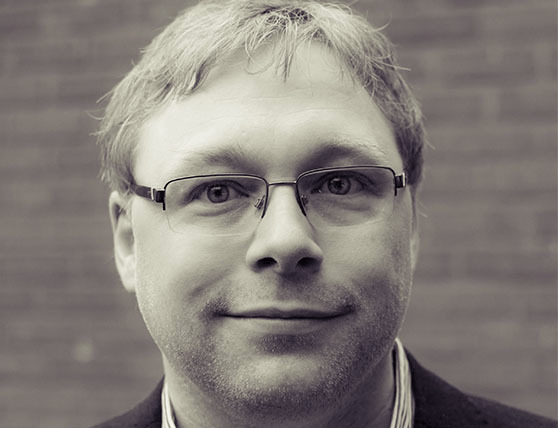 Man with glasses smiling in black and white photo.