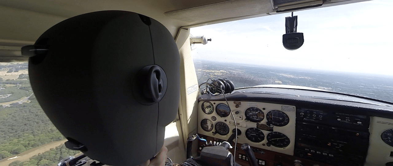 Pilot wearing VR headset in a Cessna cockpit flying over a landscape.