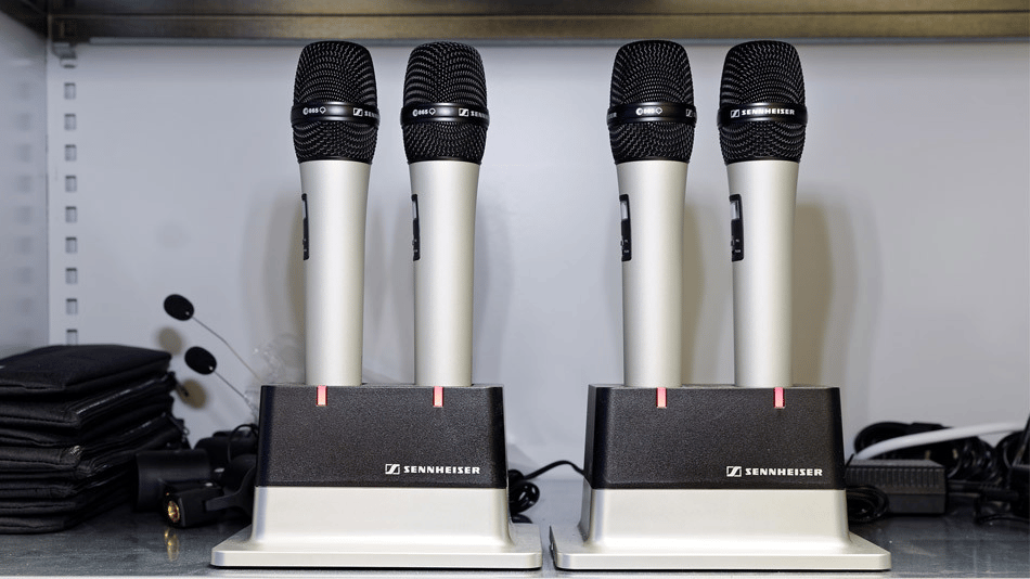 Sennheiser wireless microphones in charging stations on a shelf.