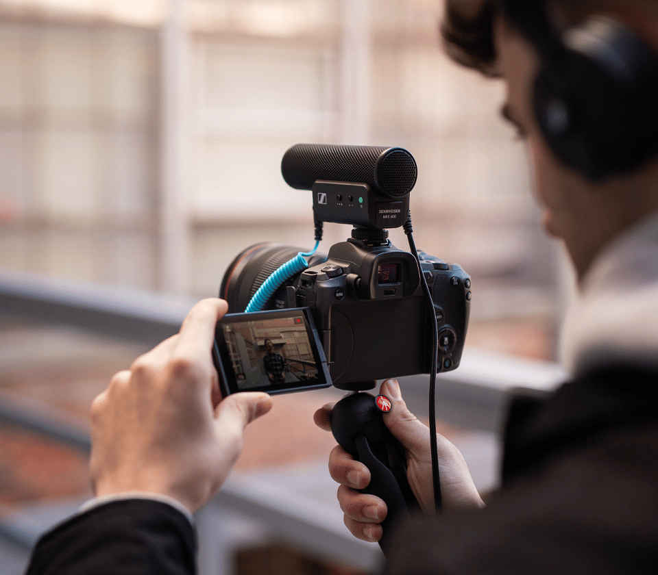 Person using a camera with a Sennheiser MKE 400 microphone attached.