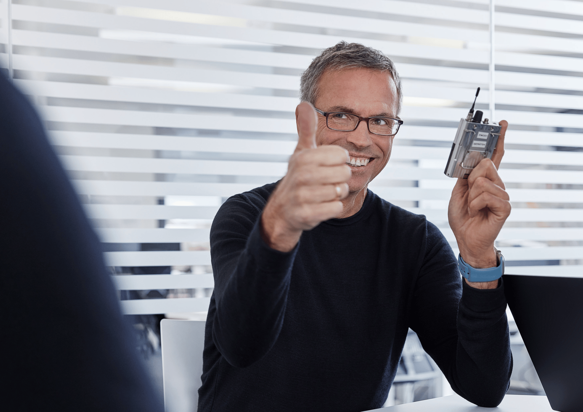 Man giving thumbs up while holding a Sennheiser wireless microphone pack.